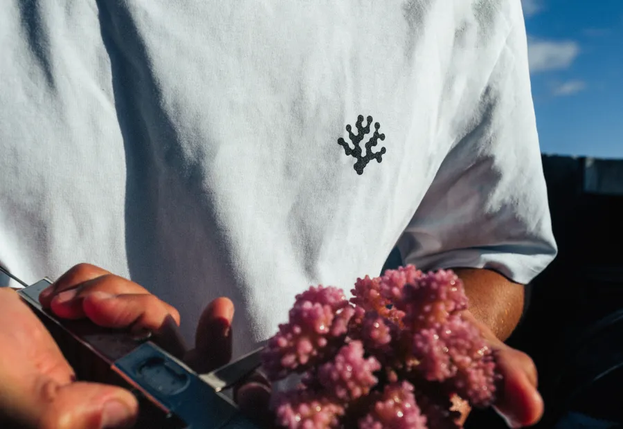 A white tee with the coral mark, a coral in hand