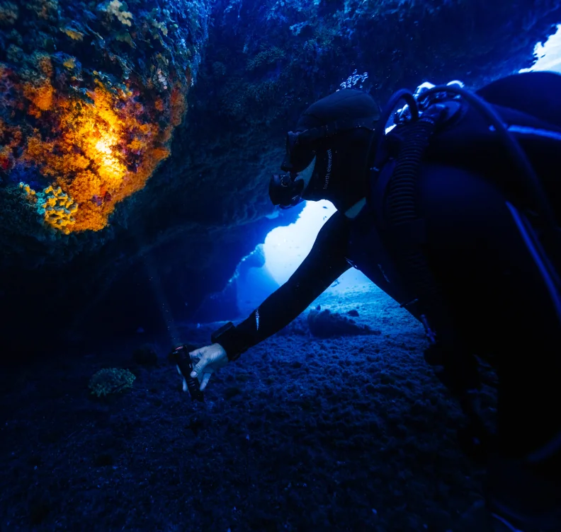A diver with a torch exploring a dark underwater cave