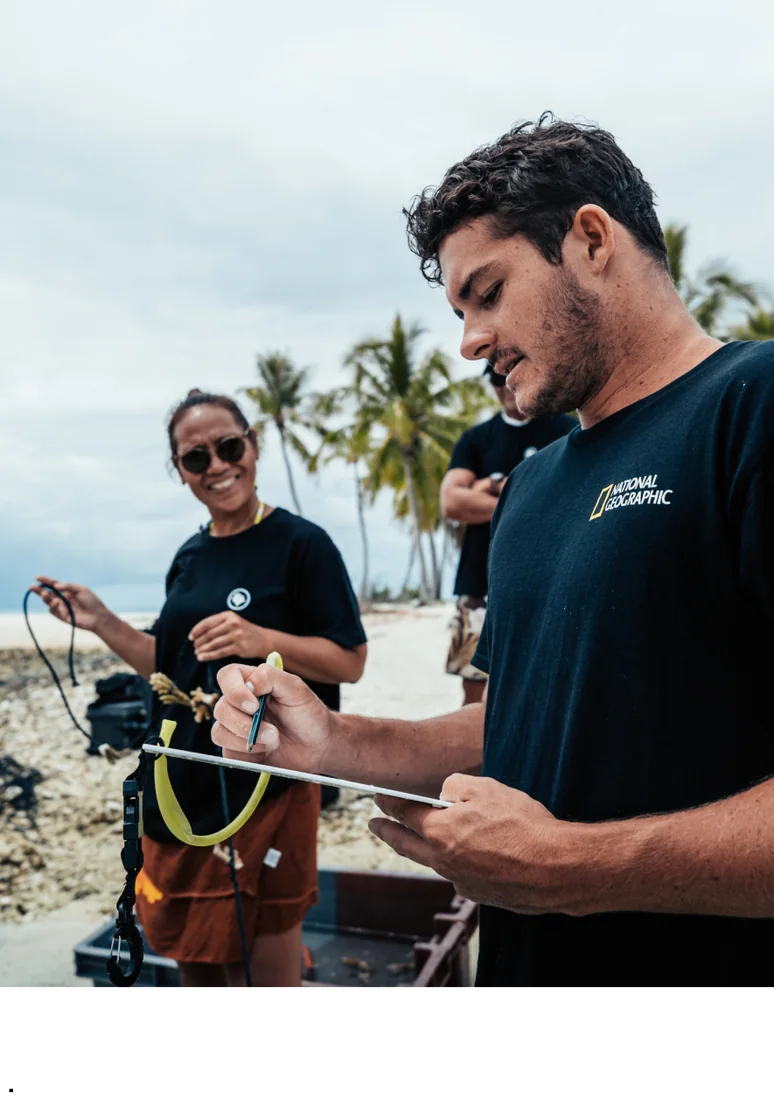 Two Gardeners preparing survey gear on the beach in National Geographic shirts