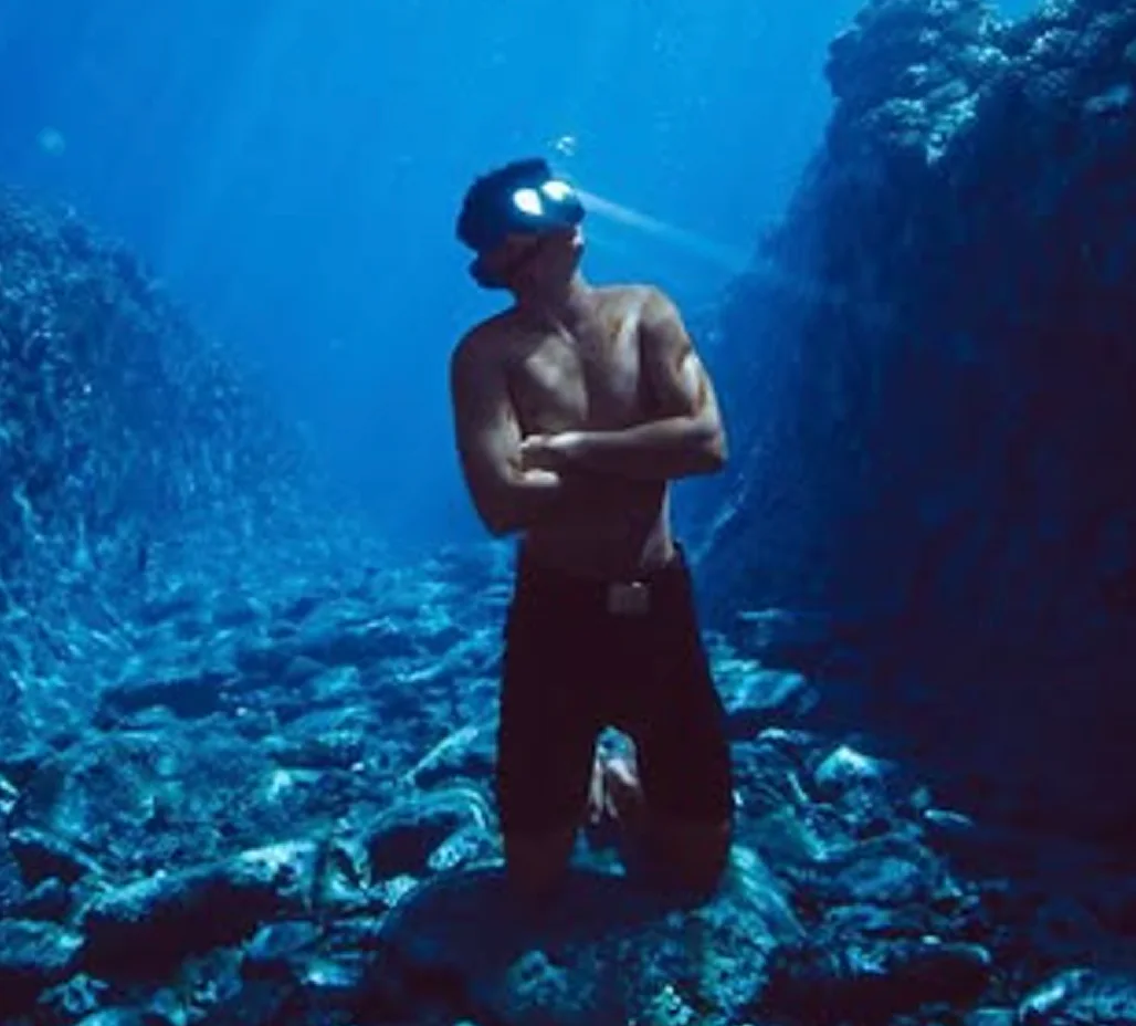 Titouan freediving between rock walls with a torch on his mask, arms folded