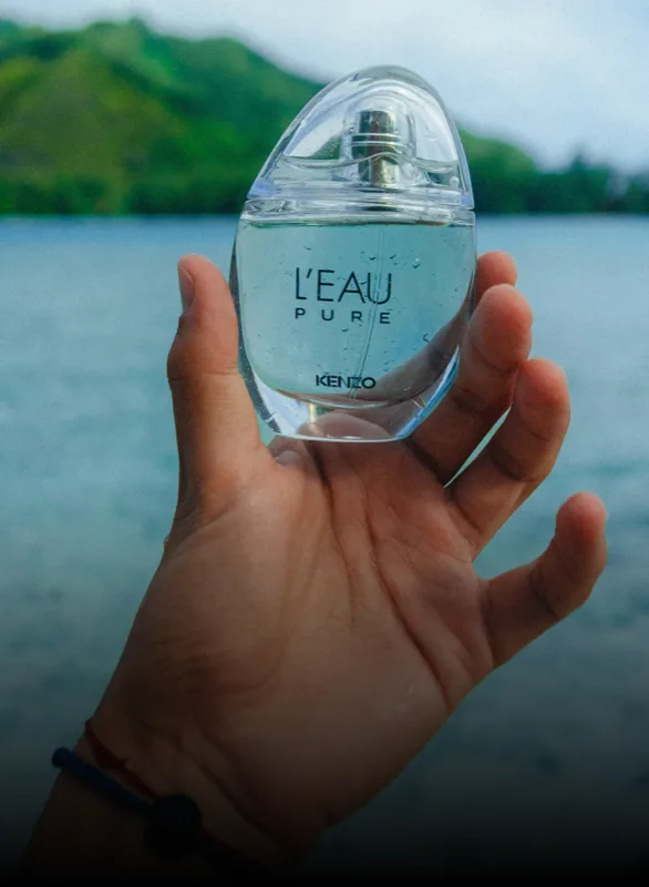 A hand holding a bottle of Kenzo L'Eau Pure over the lagoon